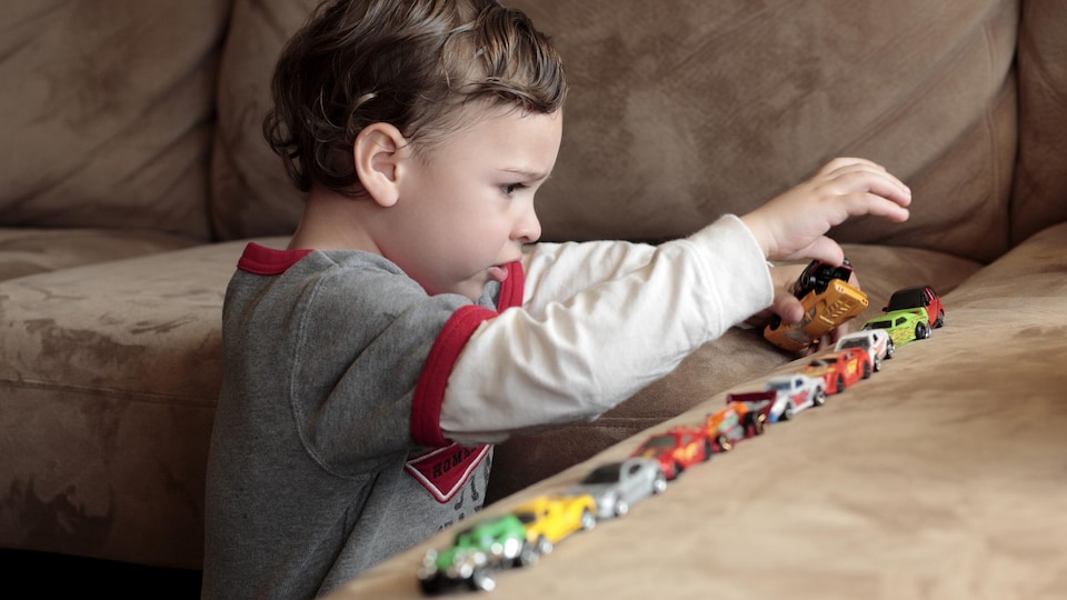Un enfant autiste joue avec des voiturettes.