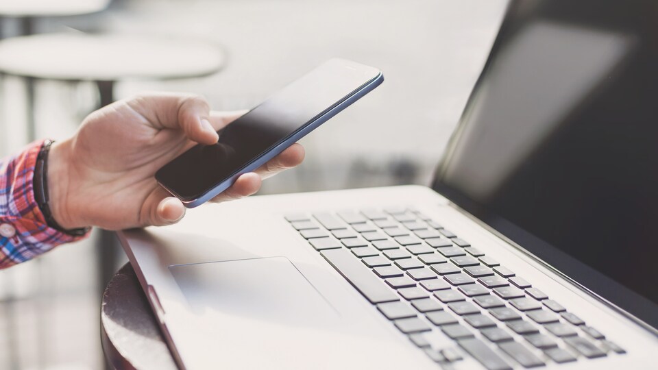 Un homme devant son clavier d'ordinateur avec son téléphone cellulaire.