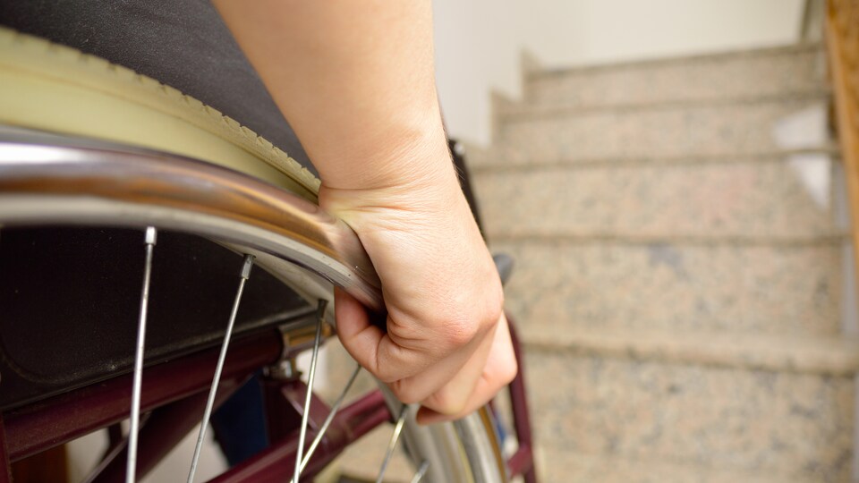 Une personne handicapée se tient devant les escaliers.
