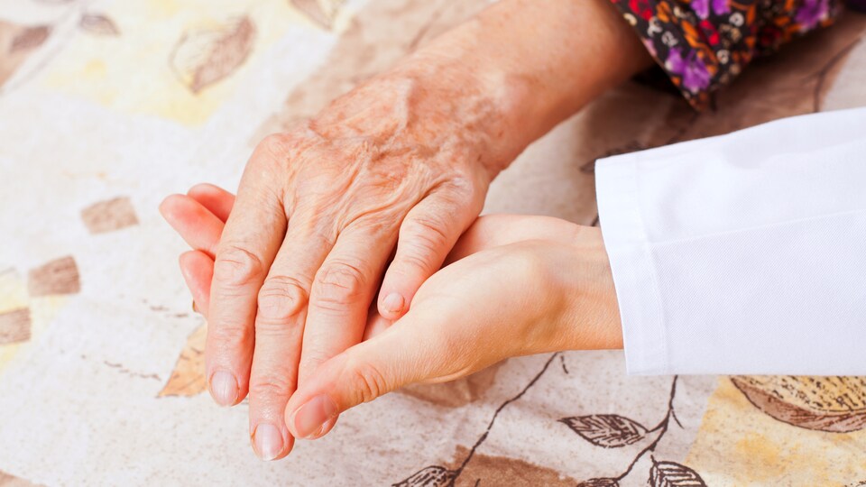 Une femme en fin de vie se fait tenir la main par une personne proche.