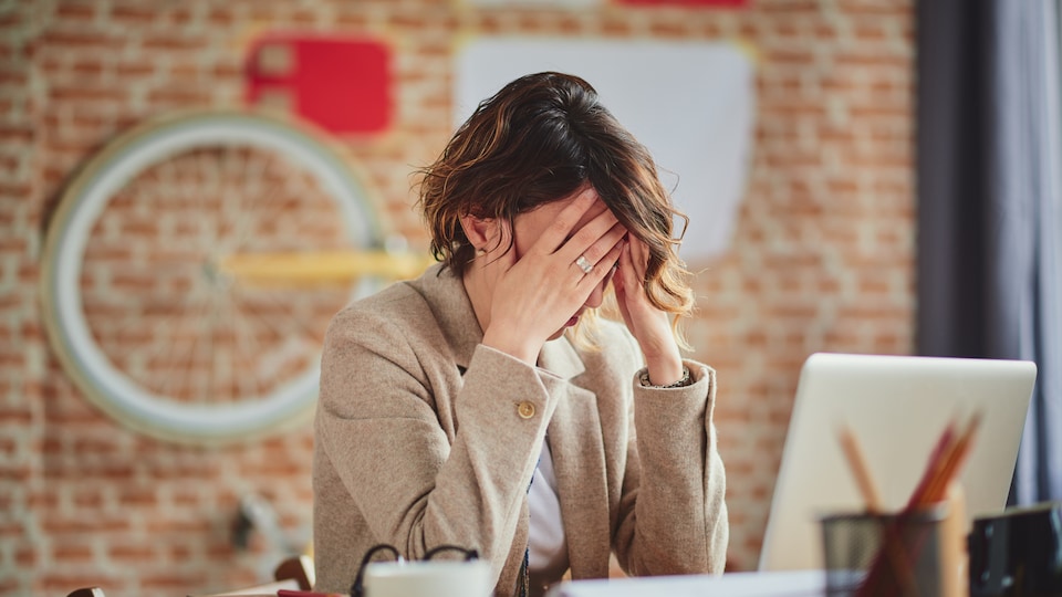 Une employée de bureau se tenant la tête devant un ordinateur.