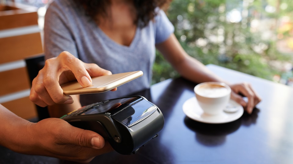 Une femme paie son cappuccino avec son téléphone intelligent.