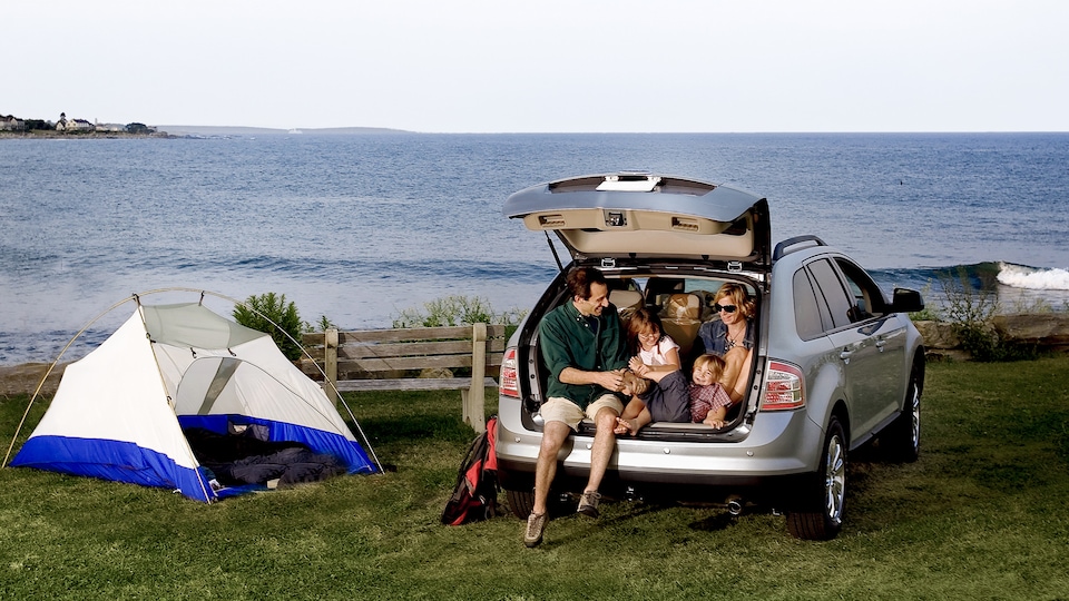Une famille assise dans l'arrière d'un véhicule utilitaire sport sur le bord de l'océan.