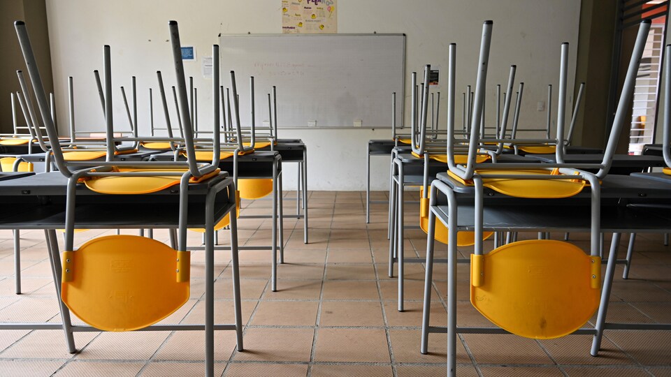 Une classe vide; les chaises sont placées sur les pupitres.