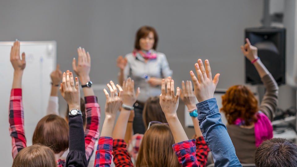 Des élèves en classe lèvent la main pour répondre à la question du professeur.