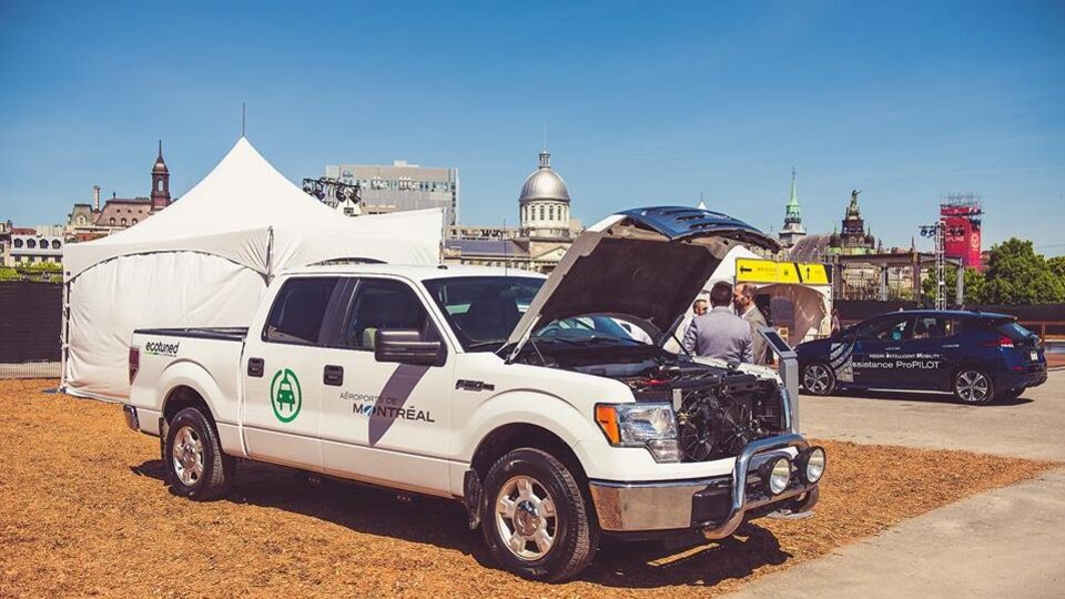 Une camionette blanche en démonstration avec le capot ouvert sous lequel l'on peut voir le moteur électrique.