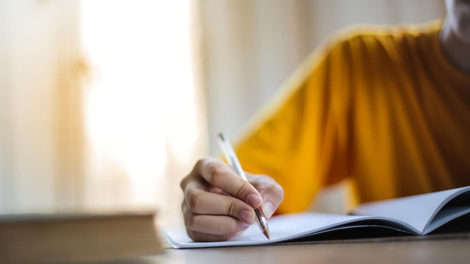 Une femme tient un stylo et écrit dans un cahier.