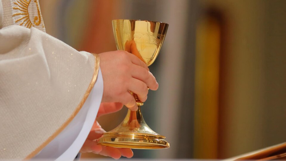 Gros plan sur les mains d'un prêtre qui tient un calice dans une église. 