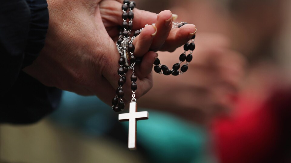 Les mains jointes, une paroissienne tient un chapelet avec une croix bien visible au bout de la chaîne.