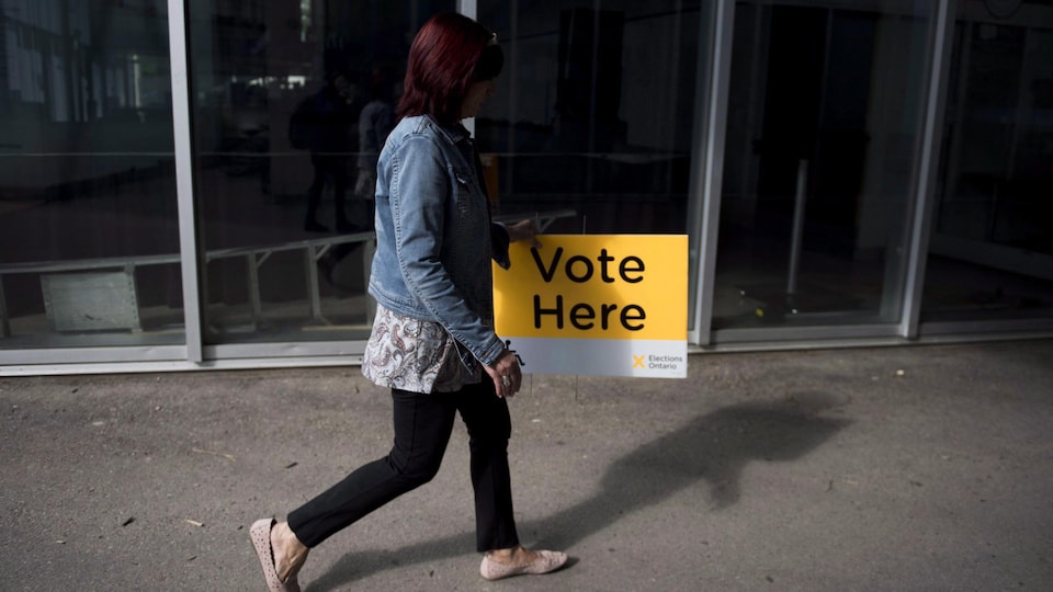 Une femme installe une pancarte à l'extérieur d'un bureau de scrutin.