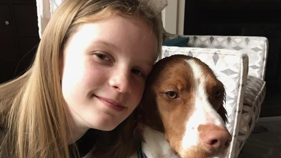 Une jeune fille aux cheveux longs, souriante, a son bras autour de son chien.
