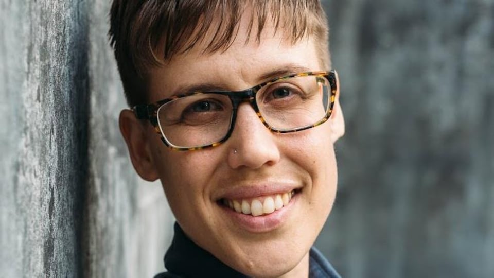 Emma Cooper est appuyée, épaule contre le mur et sourit.