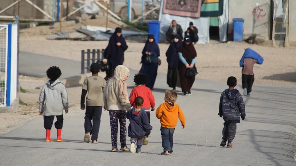 Des femmes voilées et des enfants marchent sur une route à l'intérieur d'un camp de détention. 