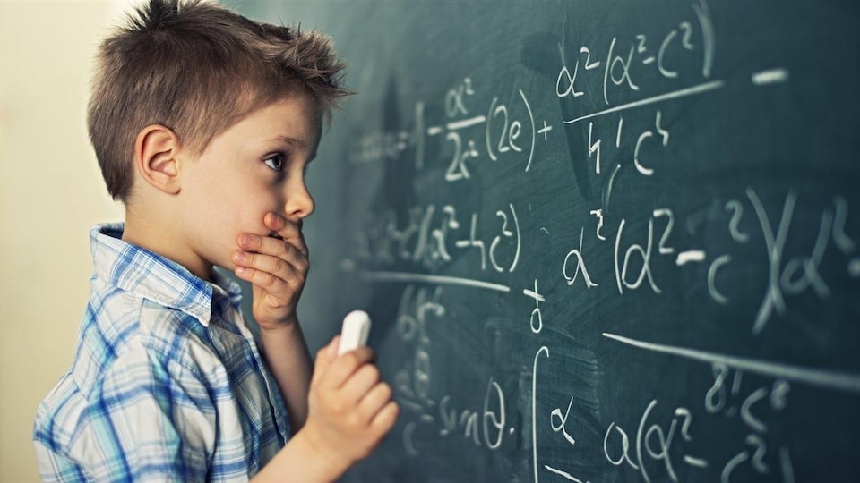 Un enfant devant un problème mathématique sur un grand tableau noir.