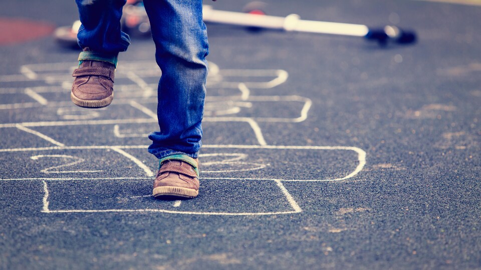 Un enfant joue à la marelle dans la rue.