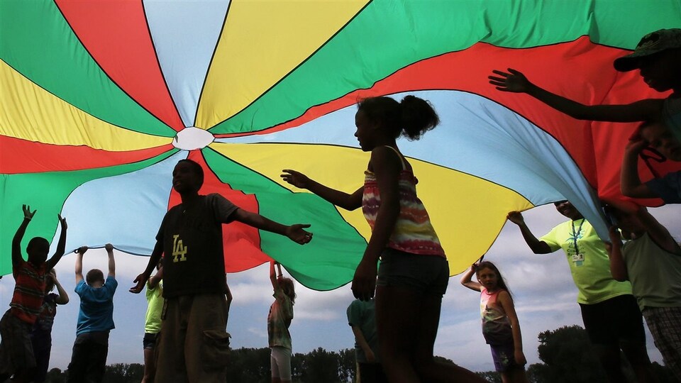 Des enfants jouent sous un grand chapiteau de tissu coloré.