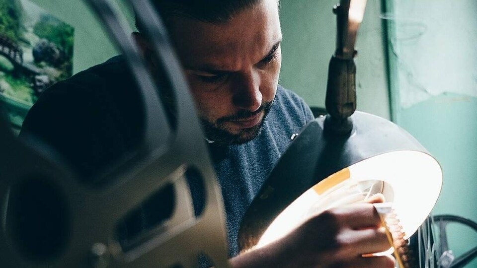 Le programmateur du cinéma Revue, Éric Veillette regarde une bobine de film sous une lumière.