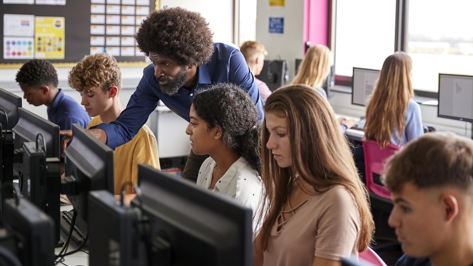 Un enseignant donne un cours à des élèves du secondaire dans une classe d’informatique.