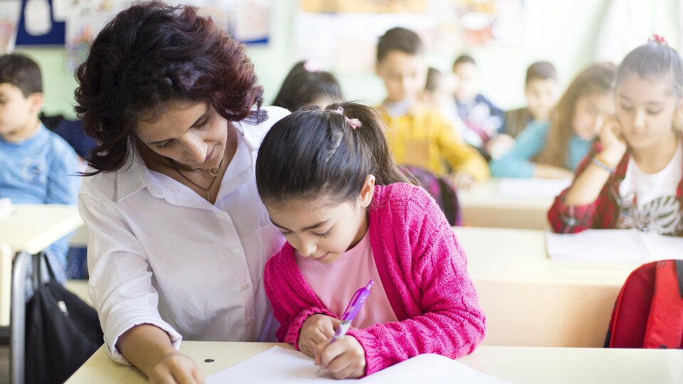 Une enseignante aide une élève qui écrit.