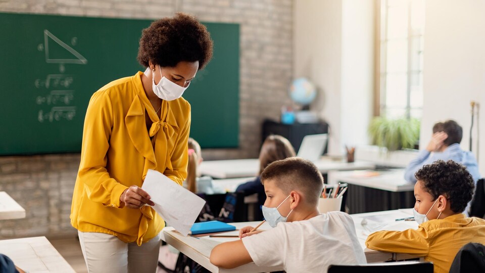 Une professeure masquée montre une feuille à l'un de ses élèves masqués, en classe, lors d'un cours de mathématiques.