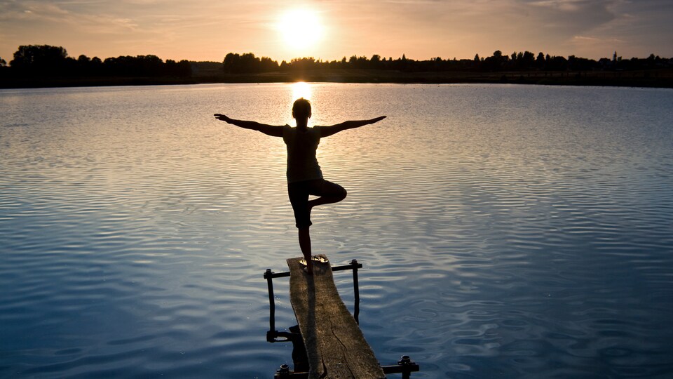 Une femme sur un petit quai de bois, dans un lac, au coucher du soleil.