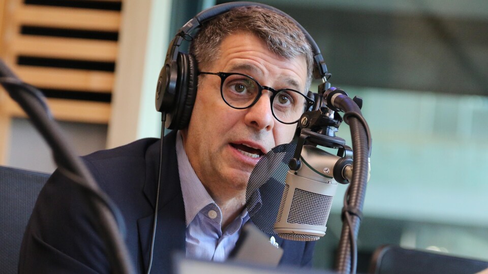 Un homme, casque d'écoute sur la tête, parle dans le micro d'un studio de radio.