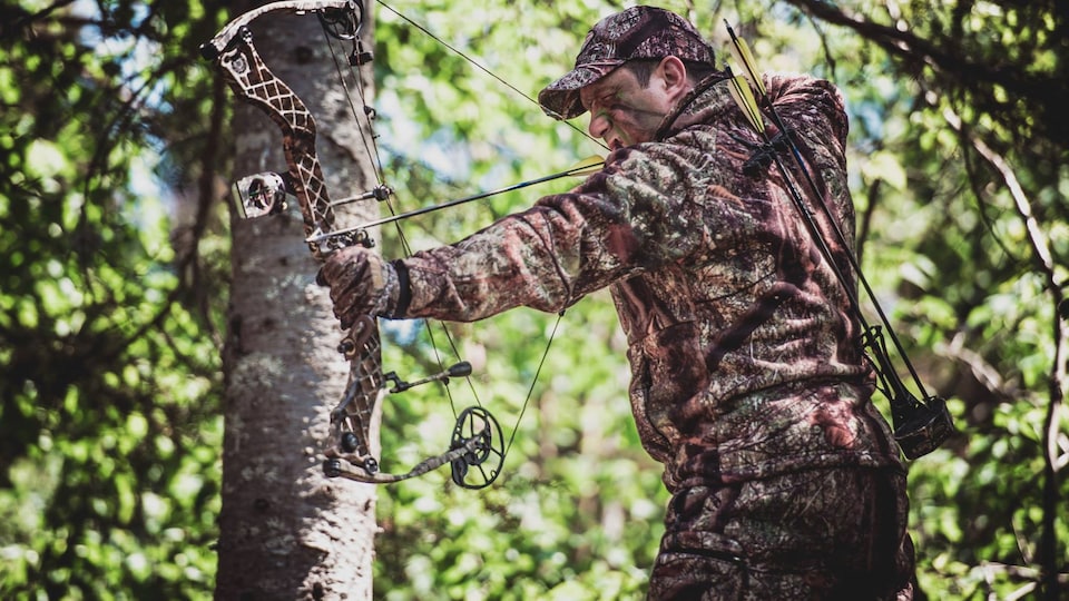 Un homme tire à l'arbalète en forêt.