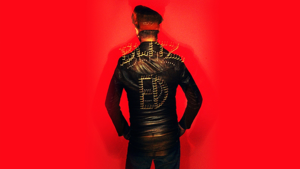 Le chanteur Étienne Daho, de dos, porte un blouson de cuir sur lequel il est inscrit « ED ».