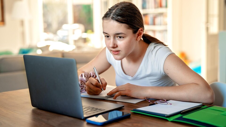 Une étudiante étudie en prenant des notes devant son ordinateur.