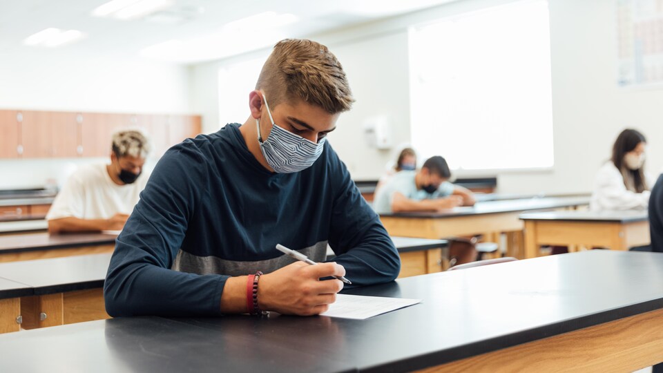 Des élèves masqués sont assis en classe à distance les uns des autres.