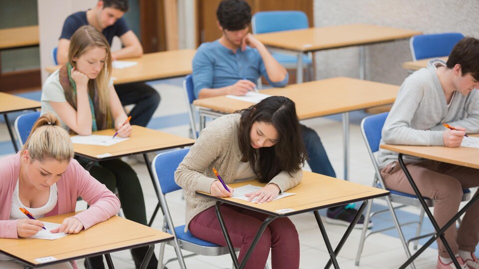 Des élèves assis à des pupitres rédigent un examen écrit. 