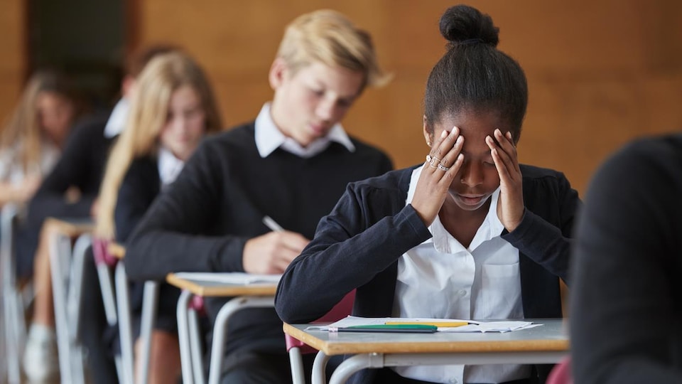 Une jeune fille assise à une table dans une salle d'examen se prend la tête dans les mains. 
