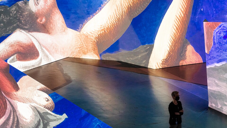 un homme marche au milieu des tableaux de Picasso projetés sur les murs dans l'exposition immersive Imagine Picasso à Vancouver