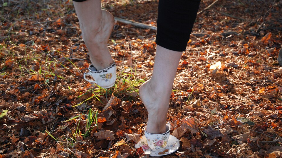 Les pieds d'une femme qui marchent dans un amas de feuilles mortes, la femme a les deux pieds dans des tasses de thé qui lui servent de souliers.