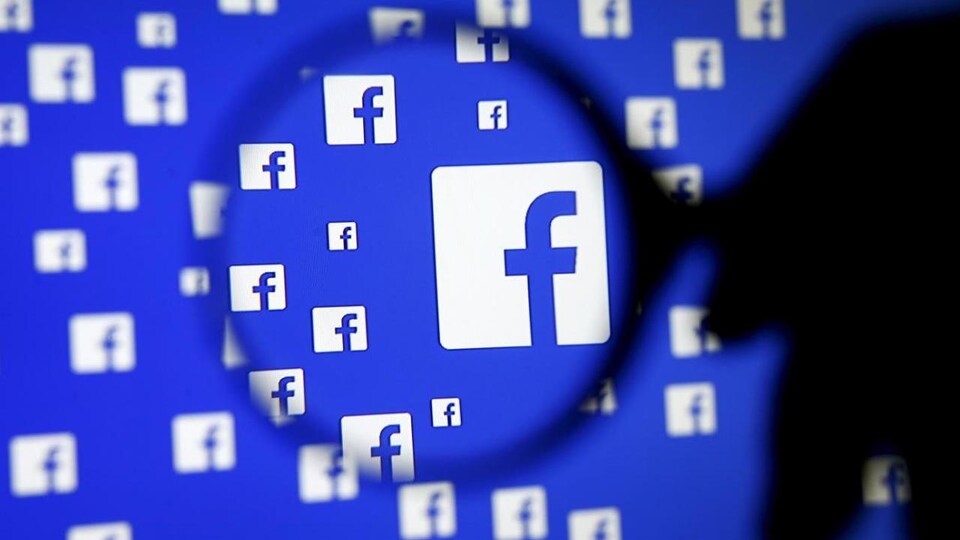 Le logo de Facebook sur un écran sous une loupe.