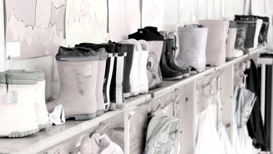Une rangée de bottes de pluies pour enfant sont affichées, à côté de bricolages et sac à dos d'enfants. 
