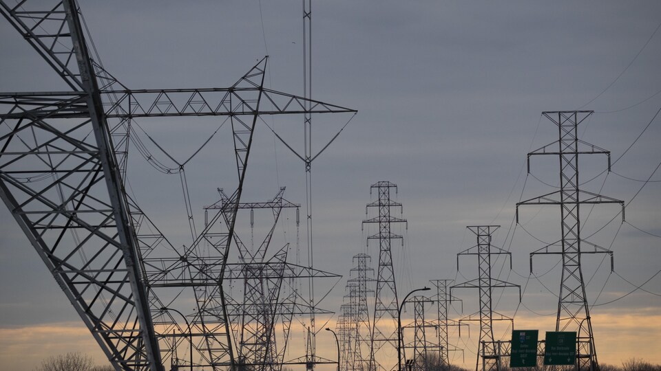 Des pylônes électriques se dressent sous un soleil couchant.