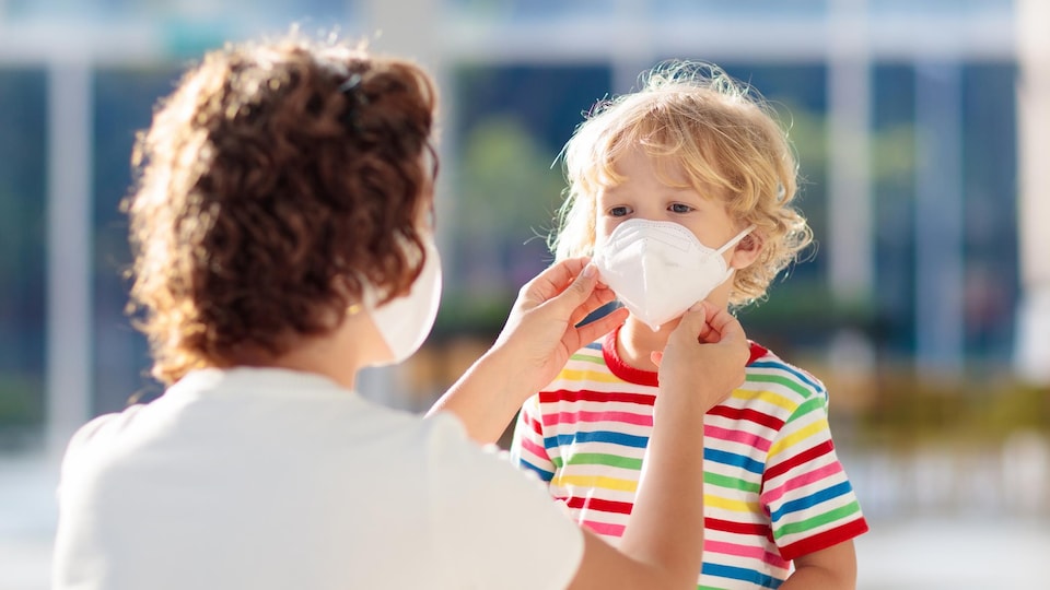 Une mère masquée installe un masque sur le visage de son fils.