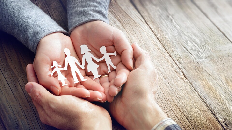 Un homme et une femme se tiennent les mains, dans lesquelles se trouvent des figurines en papier représentant les membres d'une famille.