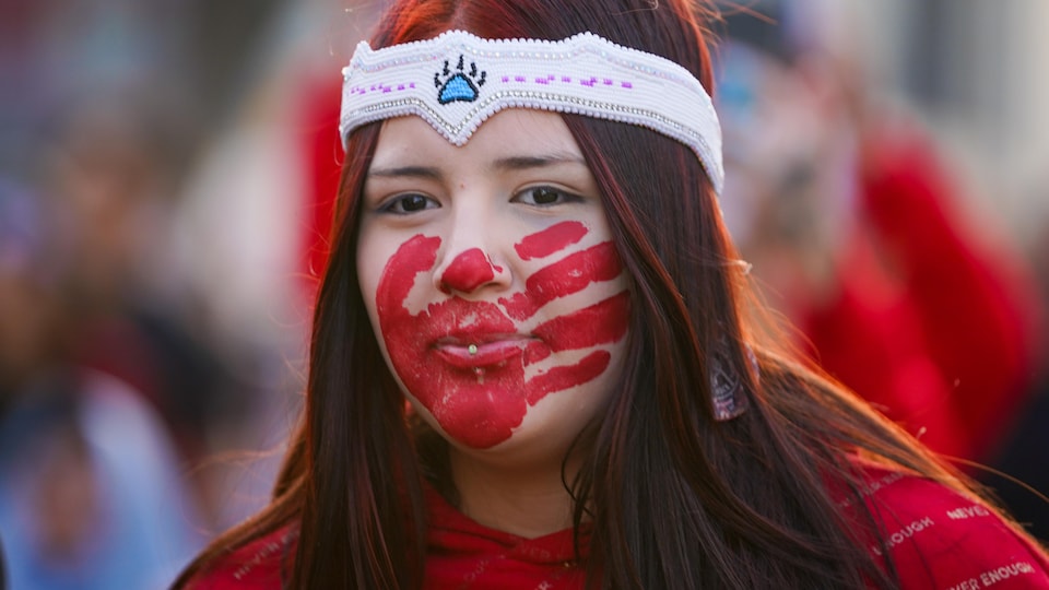Une femme porte une main rouge sur le visage lors d'une marche en mémoire des femmes et des filles autochtones disparues et assassinées à Saskatoon, en Saskatchewan, le 5 mai 2023.