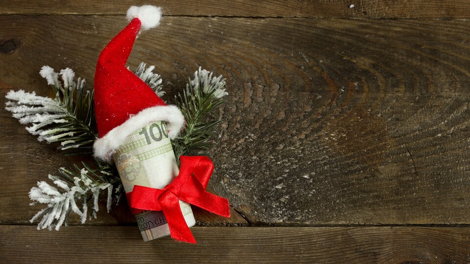 Un billet de 100 dollars déposé sur une branche de sapin, porte un chapeau de père Noël.
