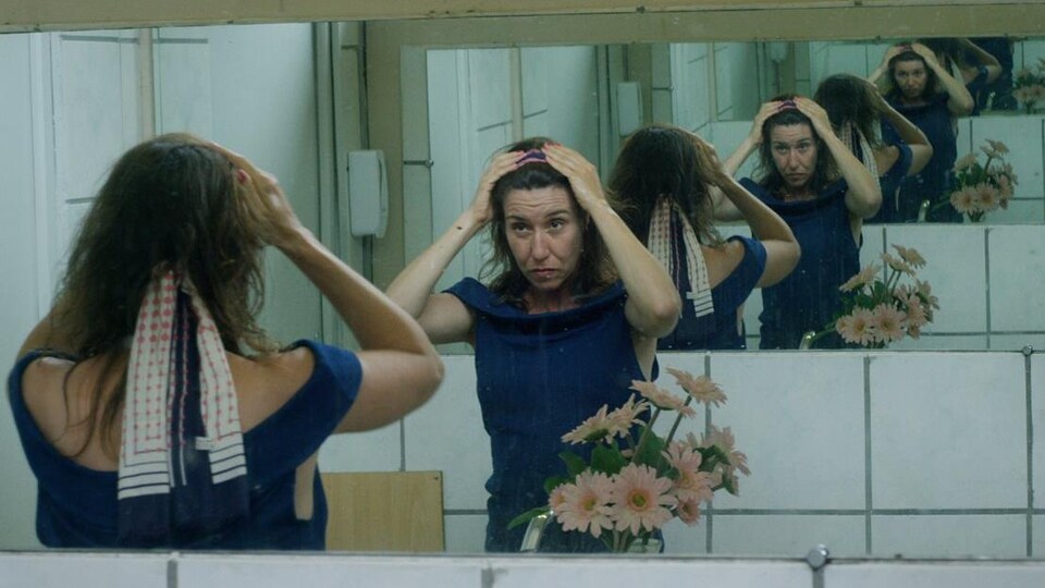 Une actrice se regarde dans un miroir l'air découragé, avec les deux mains sur sa tête.