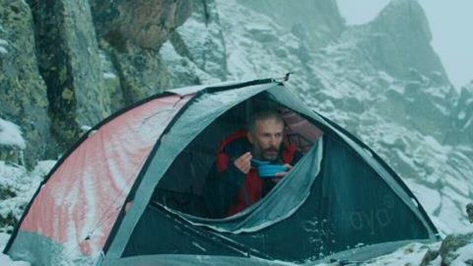 Un homme campe sous une tente dans la montagne enneigée.
