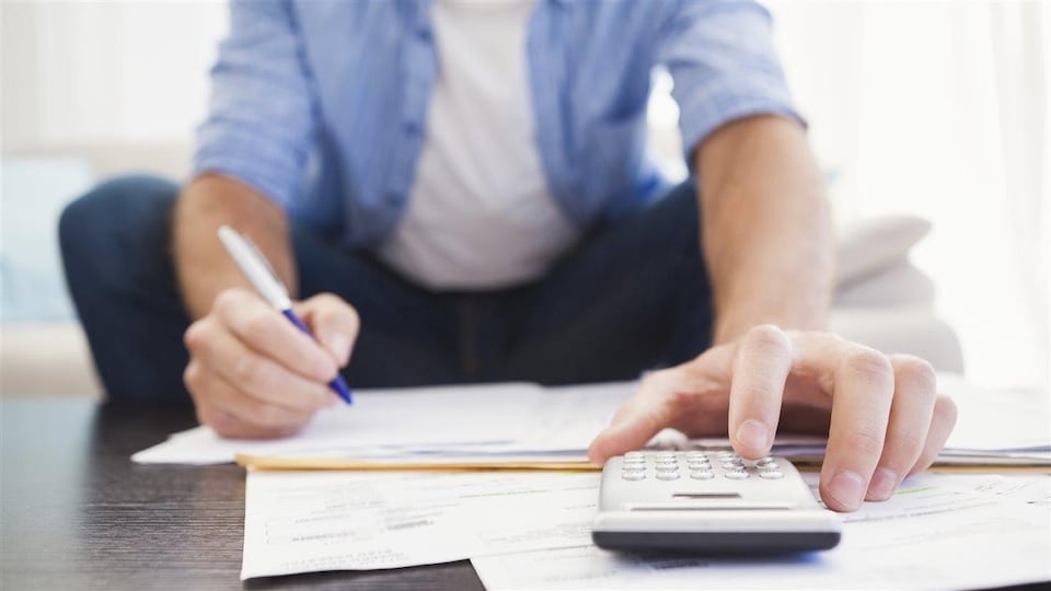 Un homme fait un budget avec une calculatrice, crayon et papier.