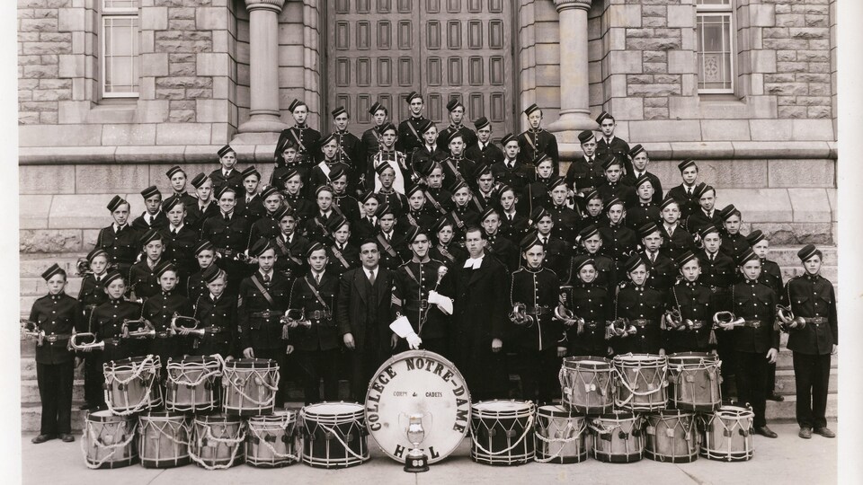 Un corps de tambour et clairons du Collège Notre-Dame à l'extérieur devant un édifice.