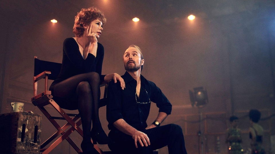 Gwen Verdon, assise sur une chaise haute, pose la main sur l'épaule de Bob Fosse qui la regarde.