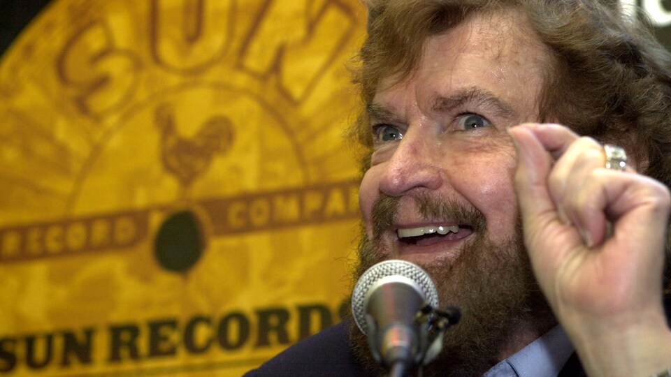 Sam Phillips sourit devant une reproduction d'un disque de Sun Records.