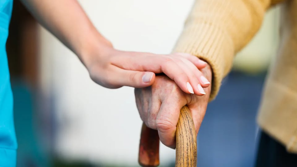 Une préposée aux soins tient la main d'une personne âgée.