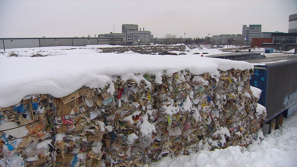 Des ballots de matières recyclables dans la neige derrière des camions, près d'un centre de recyclage à Montréal, en janvier 2018.