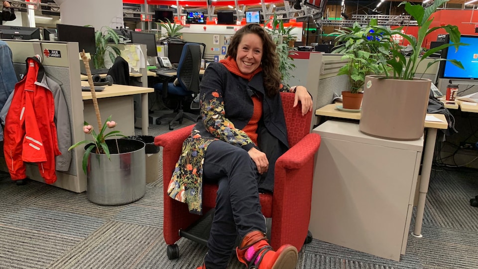 Une femme est assise sur un fauteuil rouge dans la salle de nouvelles de Radio-Canada à Vancouver.